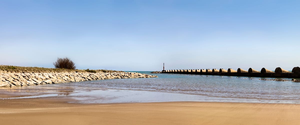 A sandy beach with a row of cylindrical concrete structures extending into the water.