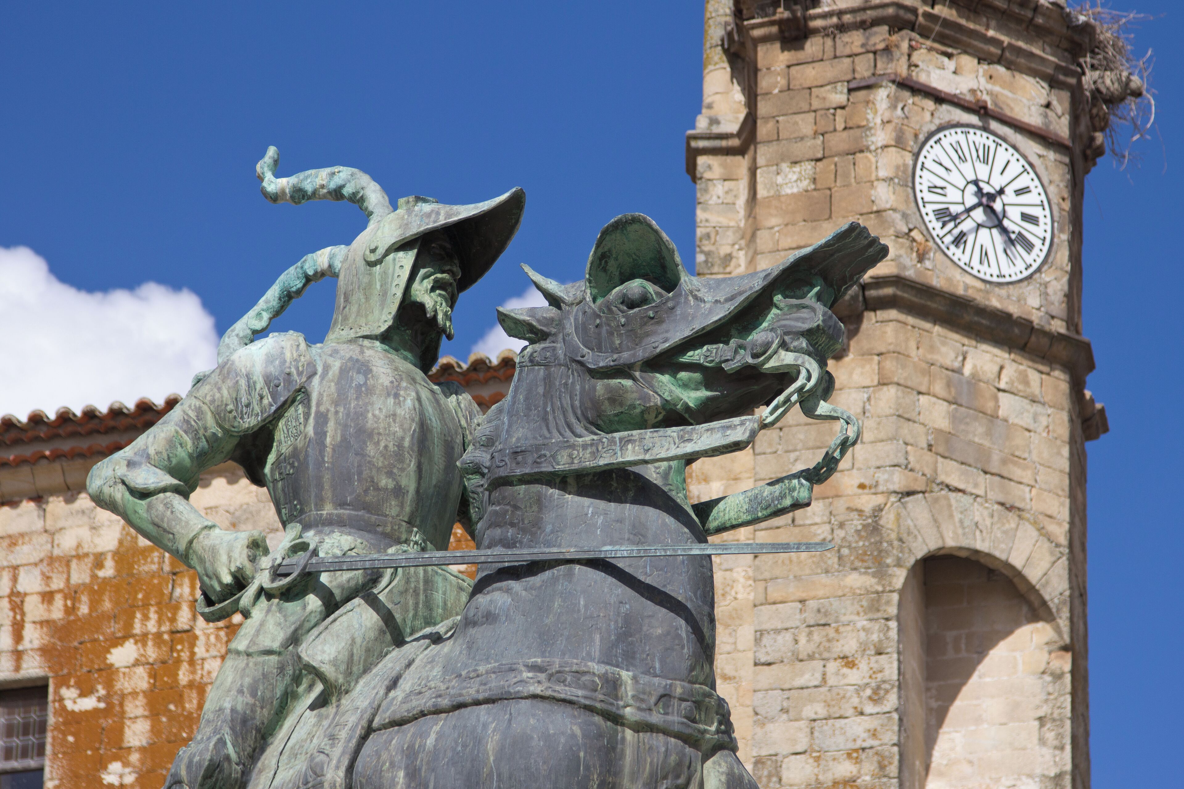 A statue of a knight on horseback in front of a clock tower.