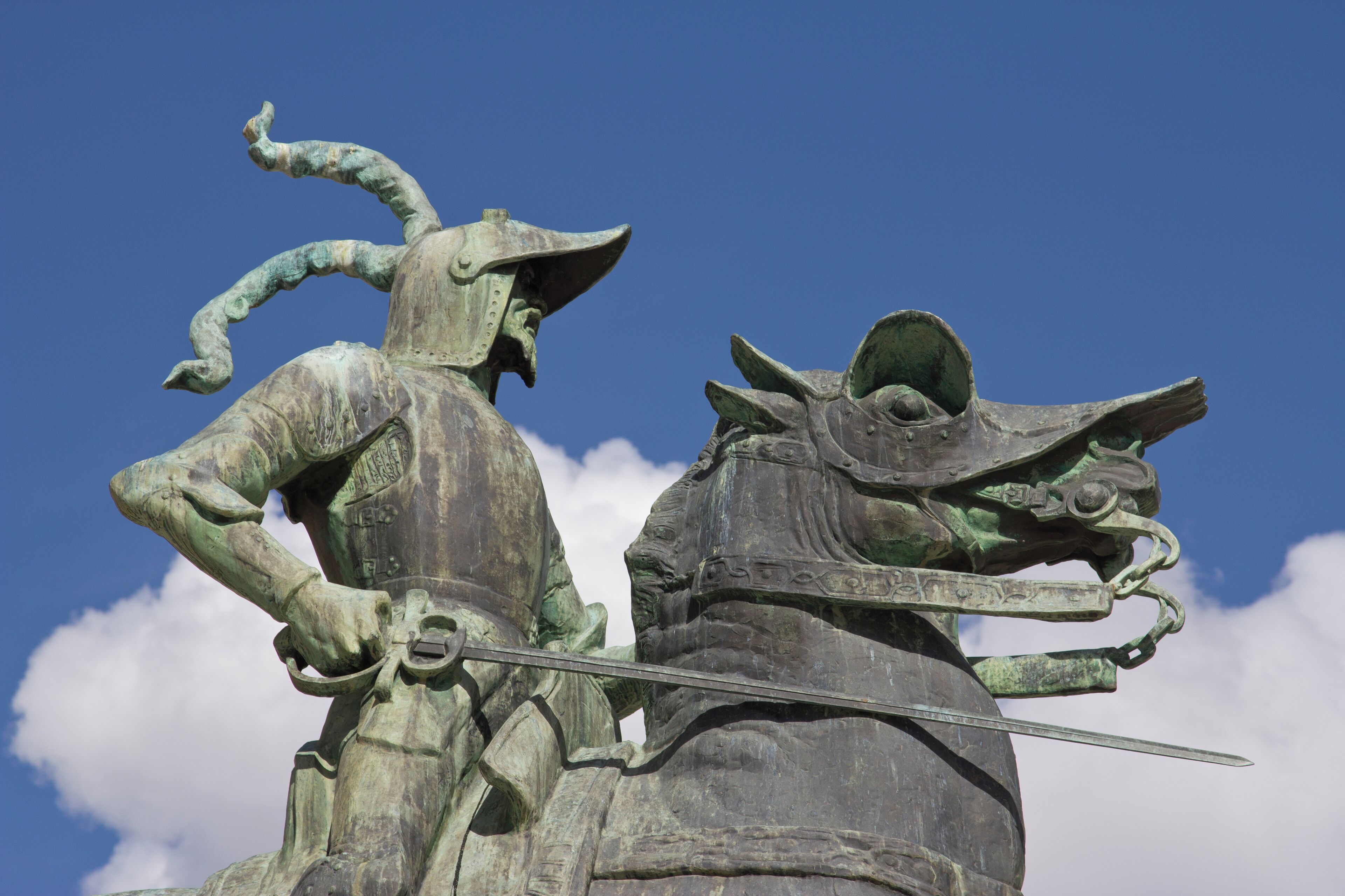 A statue of a warrior with a horse, both in bronze, against a clear blue sky.