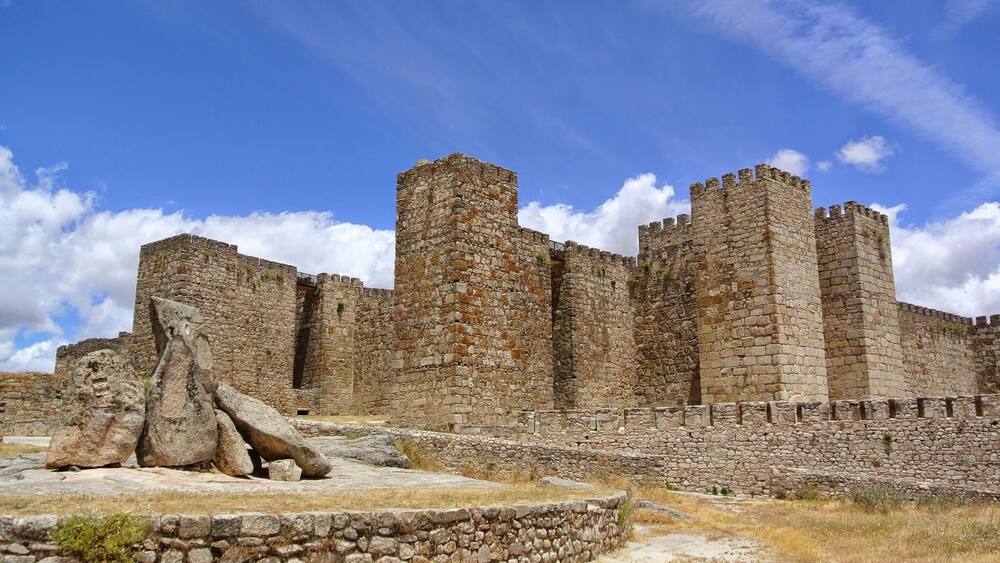 A stone castle with multiple towers and a large rock formation in the foreground.