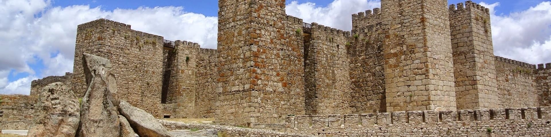 A stone castle with multiple towers and a large rock formation in the foreground.