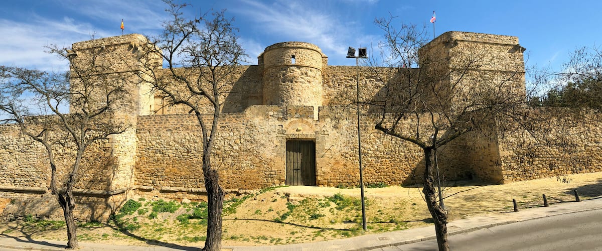 A historic stone castle with two towers, a central entrance, and a flagpole.
