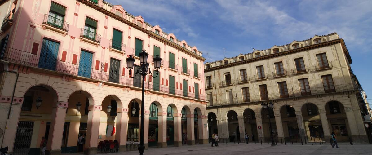 A historic square with two prominent buildings featuring arched windows and balconies.