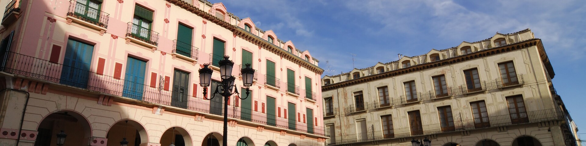 A historic square with two prominent buildings featuring arched windows and balconies.
