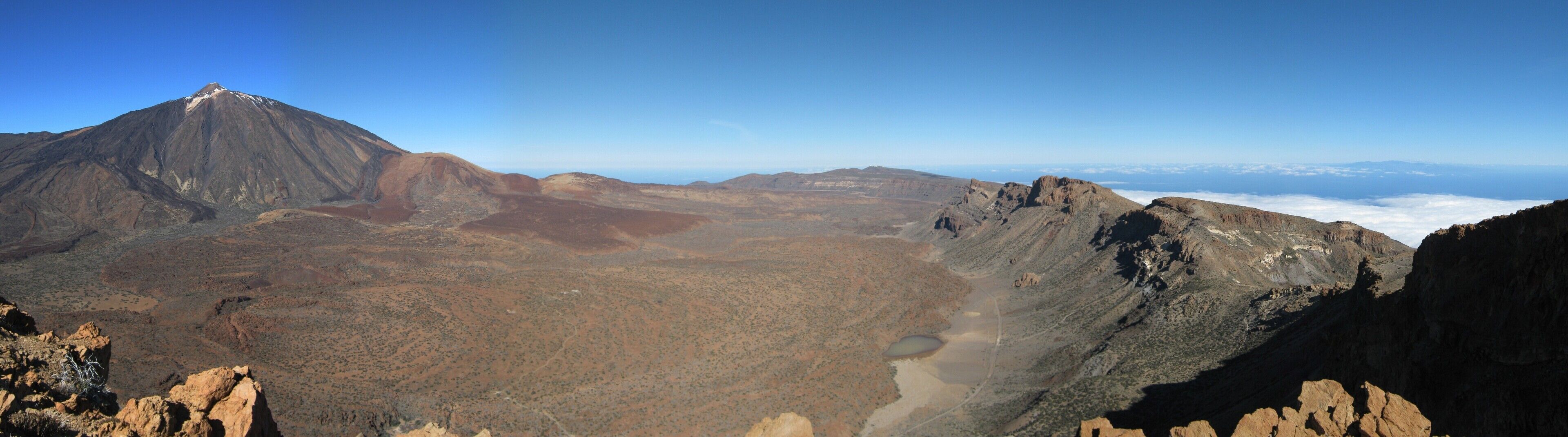 A mountainous landscape with a prominent peak, a valley, and a distant cloud-covered horizon.