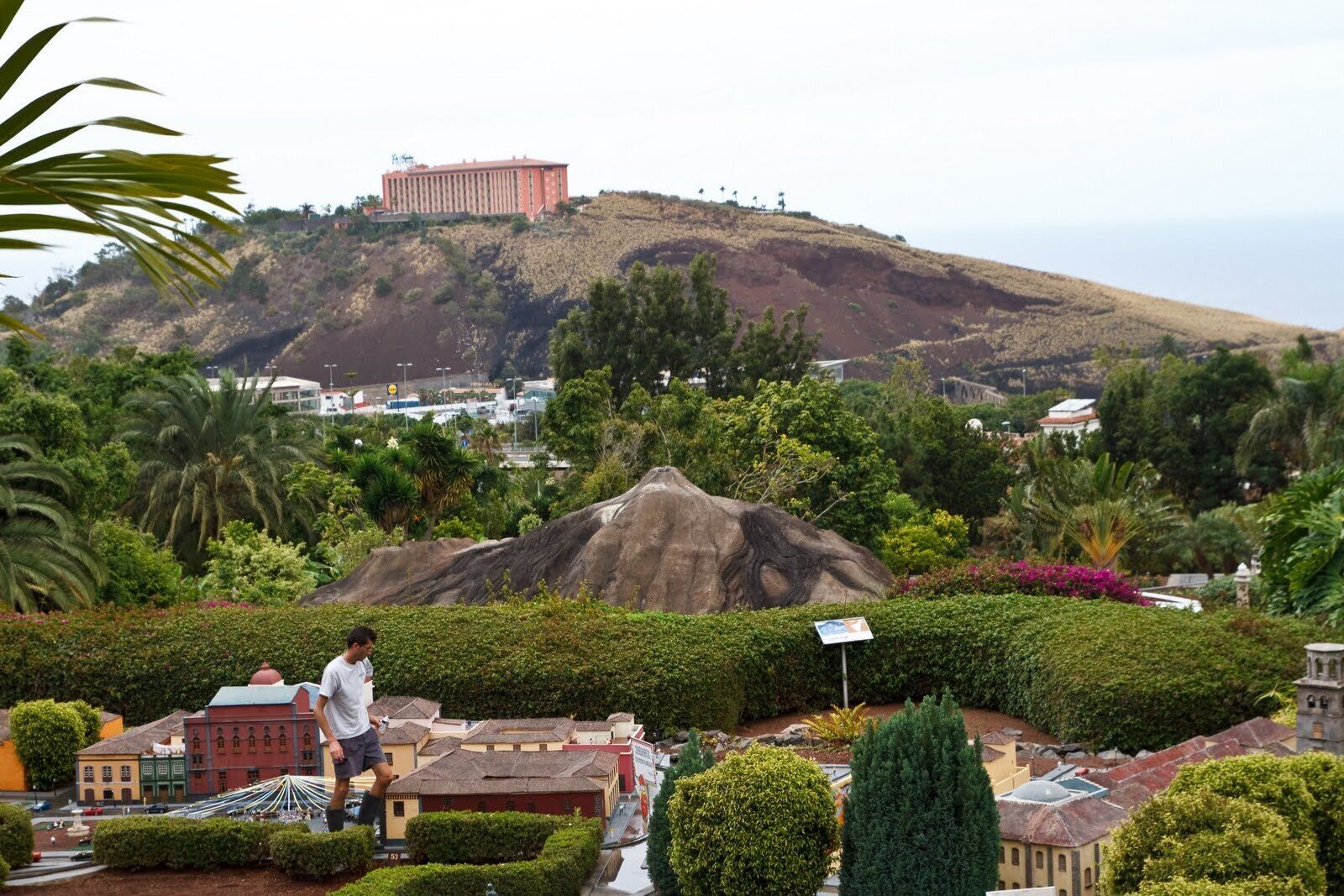 A model of a cityscape with a prominent hill in the background, a large rock formation in the foreground, and a person walking.
