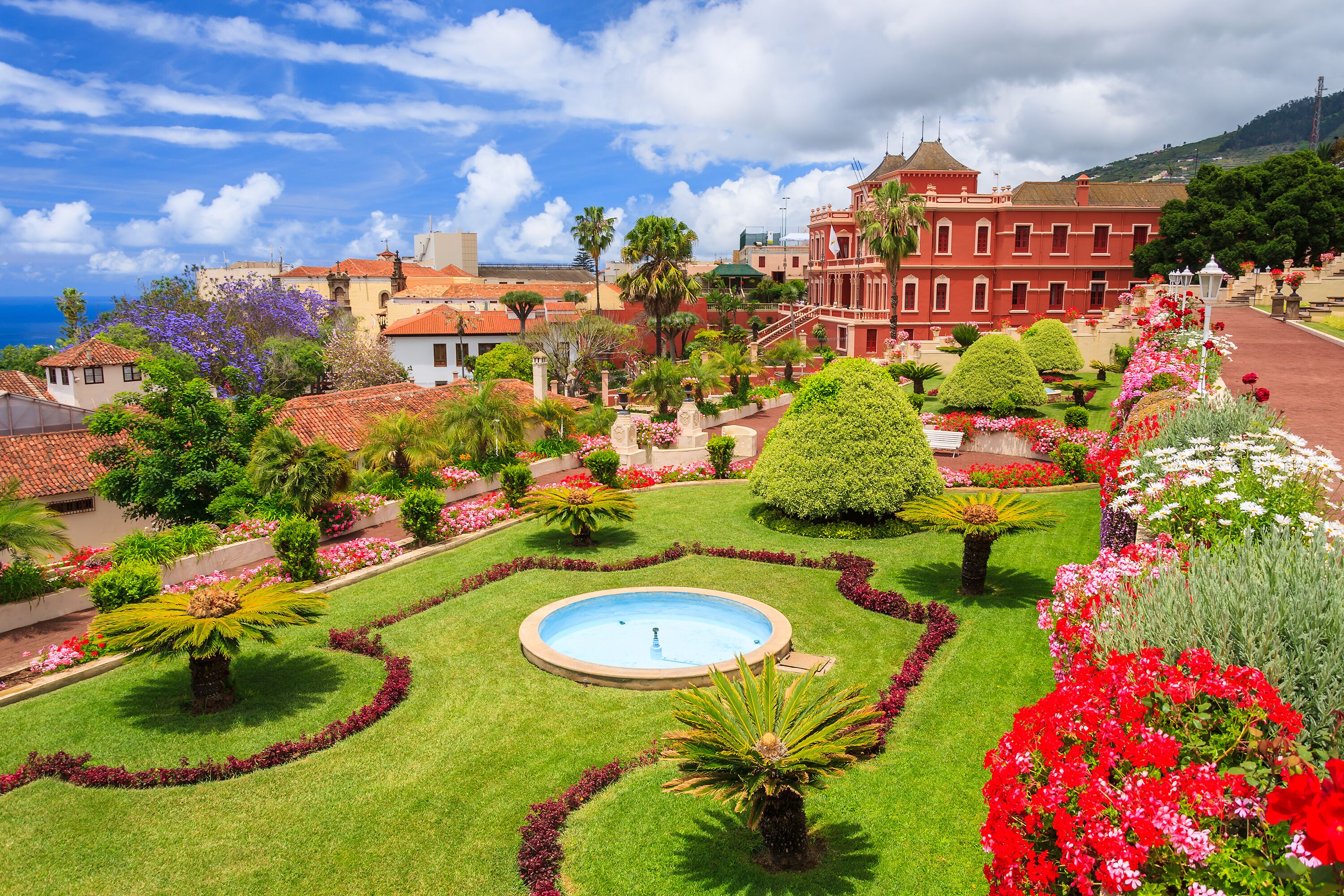 A well-manicured garden with a central fountain, surrounded by vibrant flowers and neatly trimmed hedges.