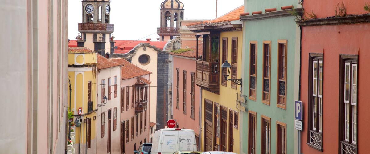 A narrow street lined with colorful buildings, a clock tower, and parked cars.