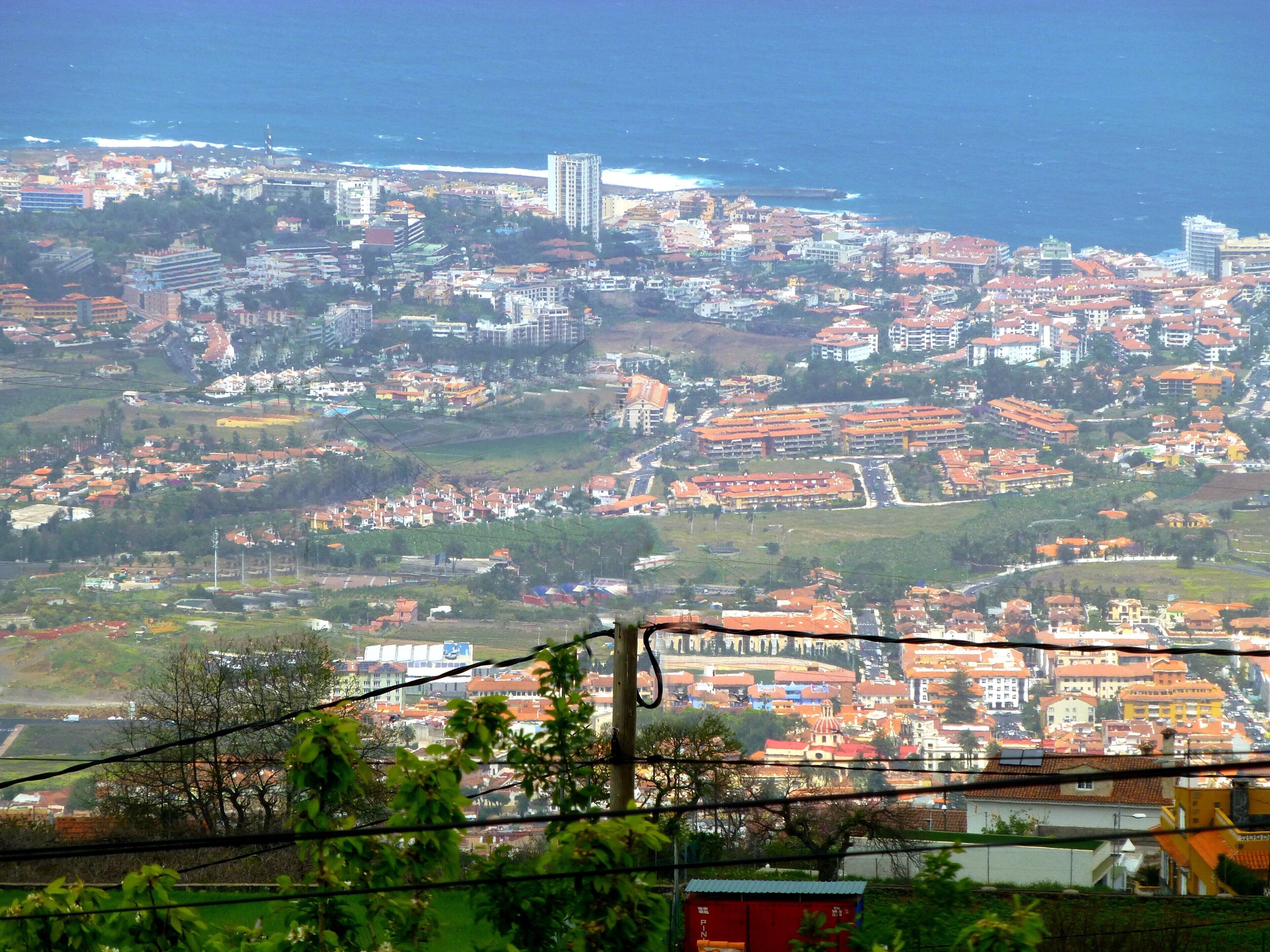 A coastal cityscape with dense housing, a prominent tall building, and a beach in the distance.