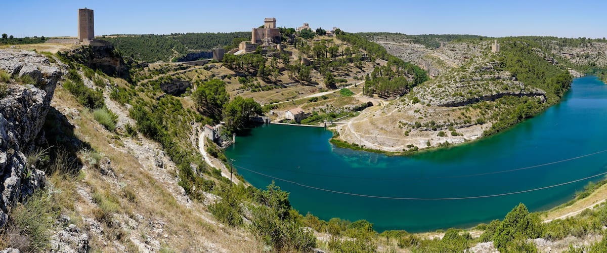 A river winding through a hilly landscape with a castle and tower on a hill.