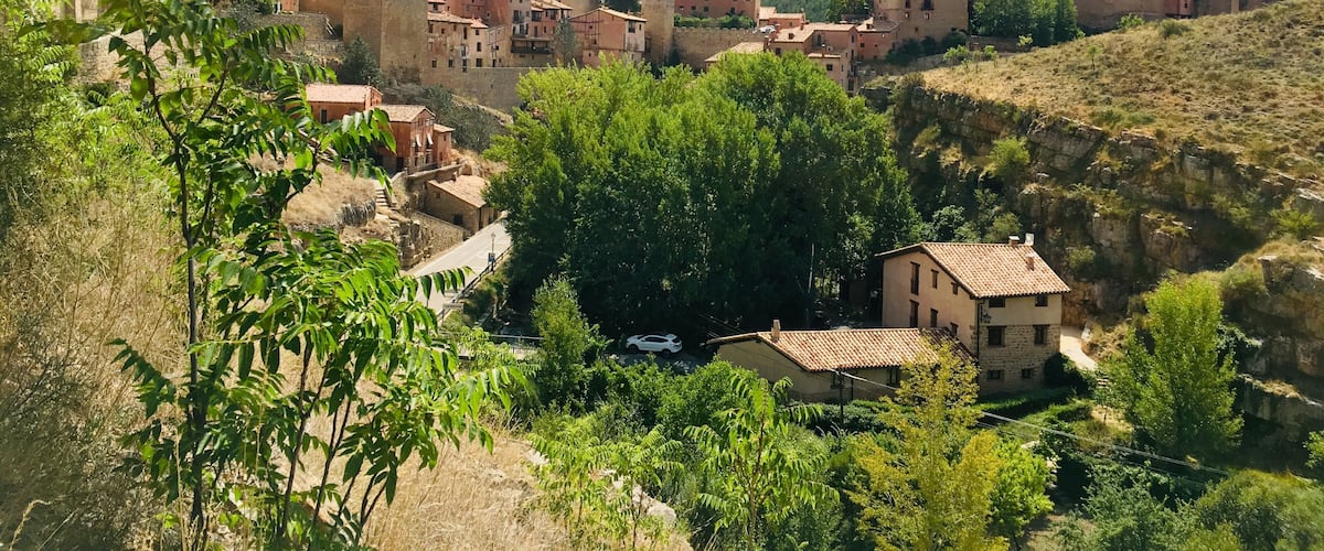 A village with terracotta-roofed buildings nestled in a valley, surrounded by greenery and hills.