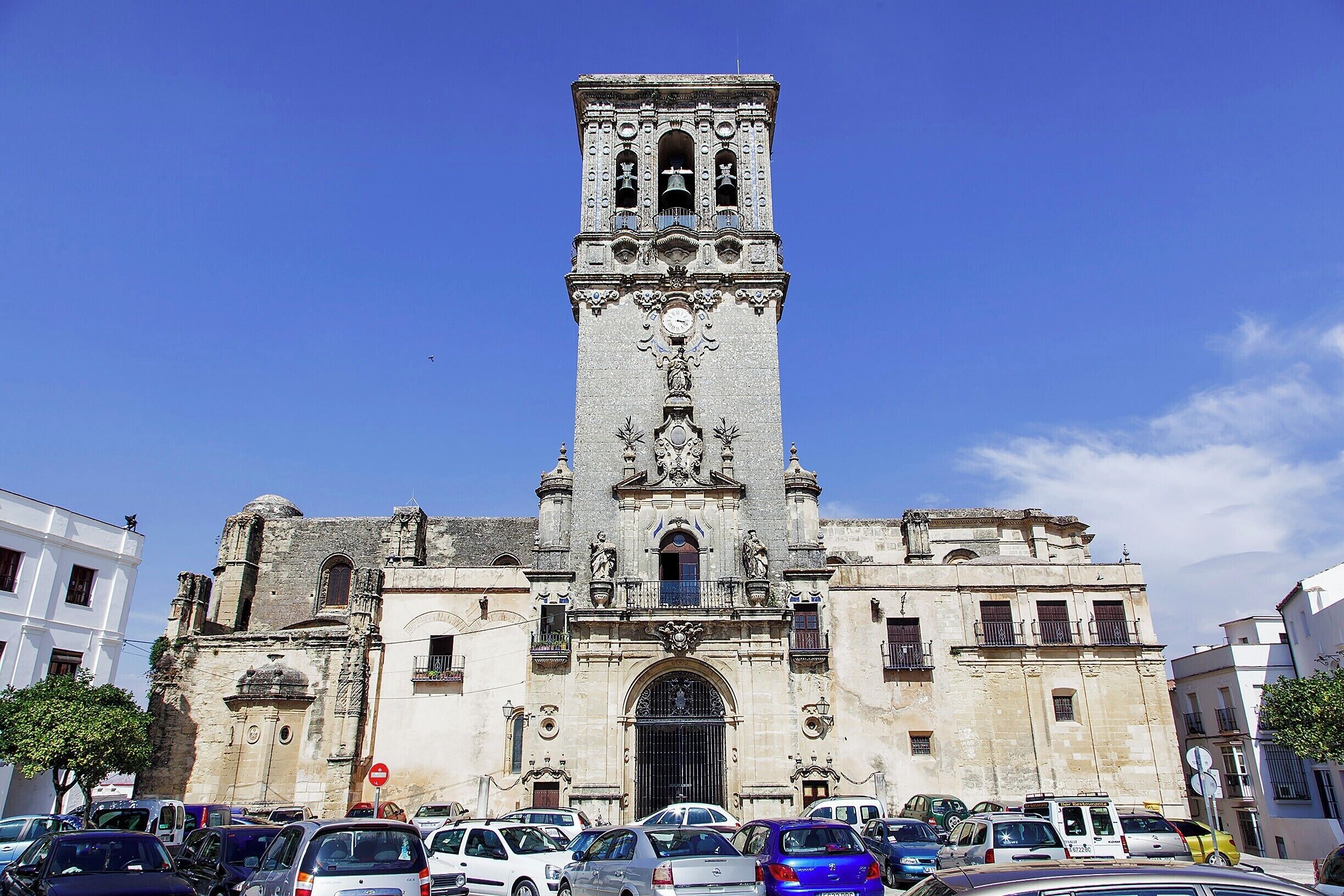 At the apex of Arcos' old town stands this odd 16th-century church.  The building dates from the 14th century, but when renovations were performed in the 16th century the outdated Mudejar style was jettisoned in favor of late Gothic, including an ornate Plateresque doorway on the west side.  In the 18th century a Baroque belfry was added, completing this eclectic church.

Unfortunately, the large town square in front of the church has been repurposed as the town's largest car park, marring the view a bit.