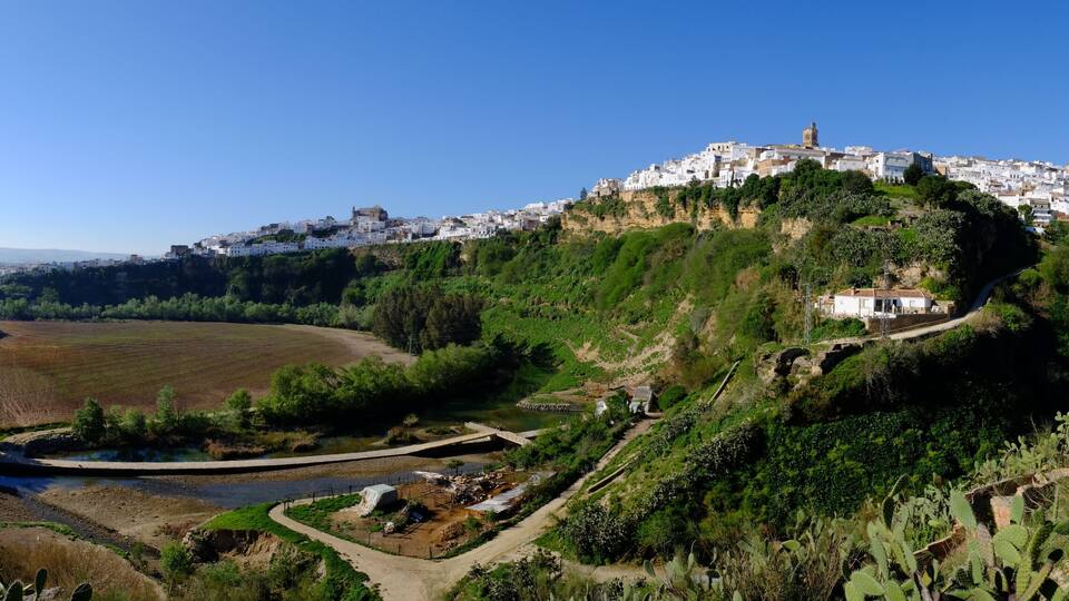 A coastal town with white buildings on a hill, a river, and surrounding greenery.