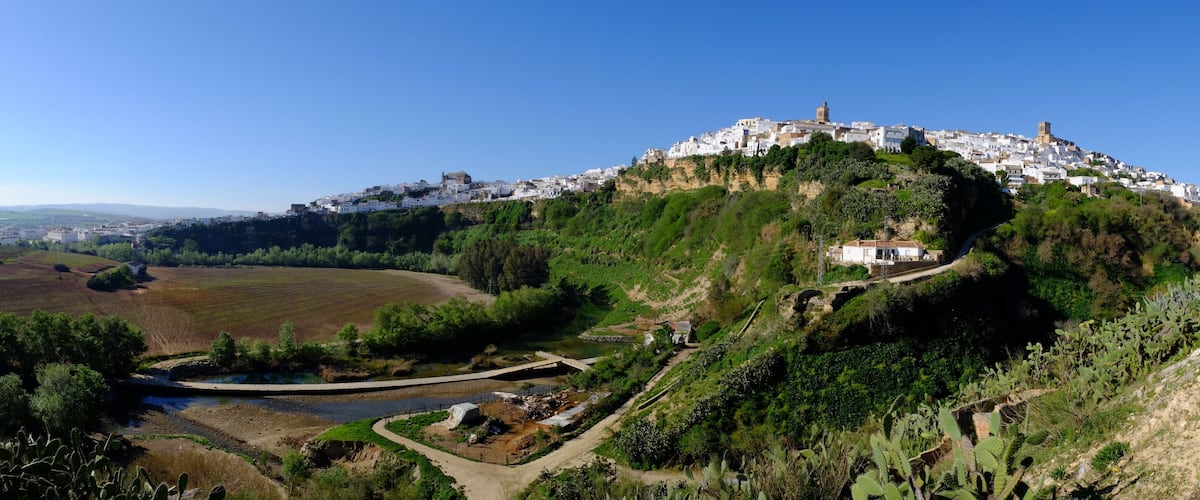 A coastal town with white buildings on a hill, a river, and surrounding greenery.