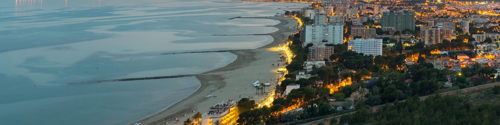 A coastal cityscape with a beach, buildings, and mountains in the distance.