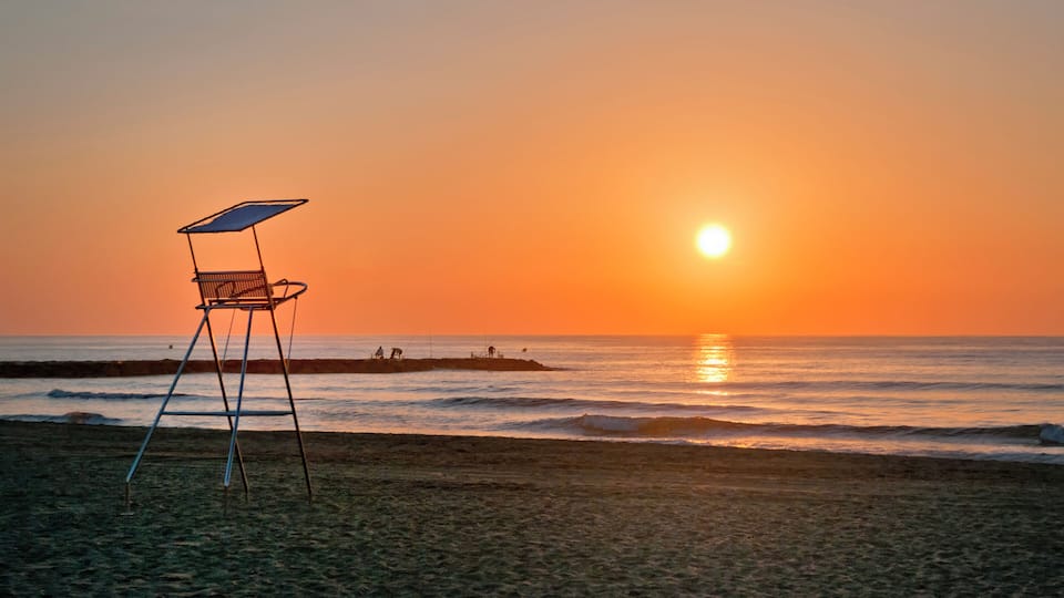 A beach chair at sunset with the ocean and a rocky outcrop in the background.