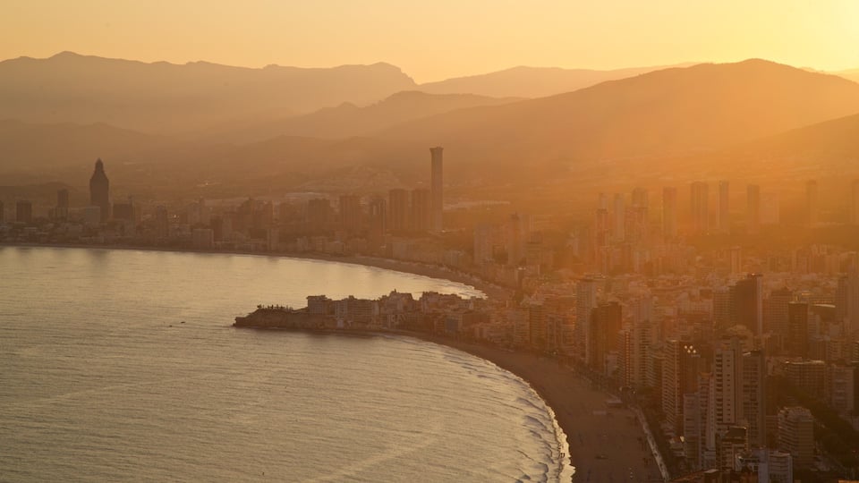 A coastal cityscape with a prominent tower, a curved coastline, and distant mountains.