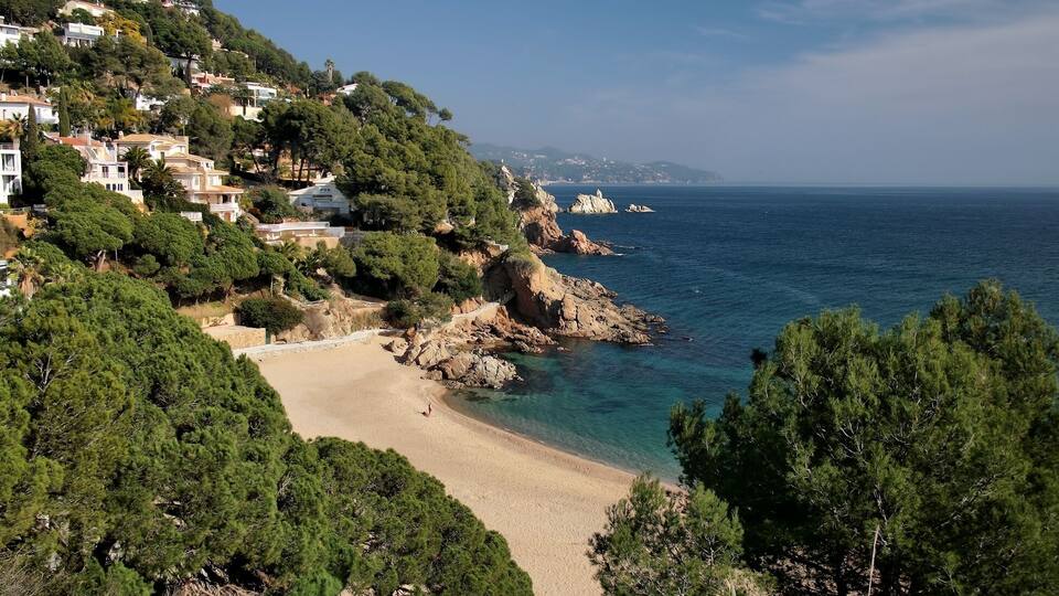 A coastal town with a sandy beach, rocky cliffs, and dense greenery.