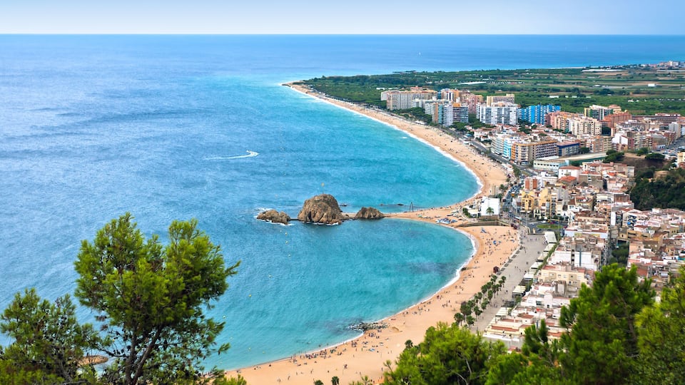 A coastal city with a beach, clear blue waters, and a rocky outcrop.