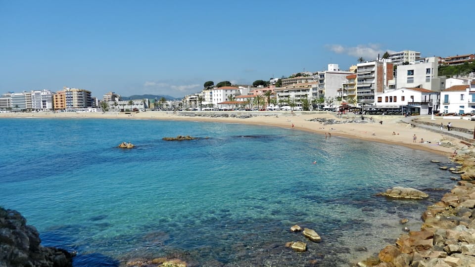A coastal town with clear blue waters, rocky shoreline, and buildings along the beach.