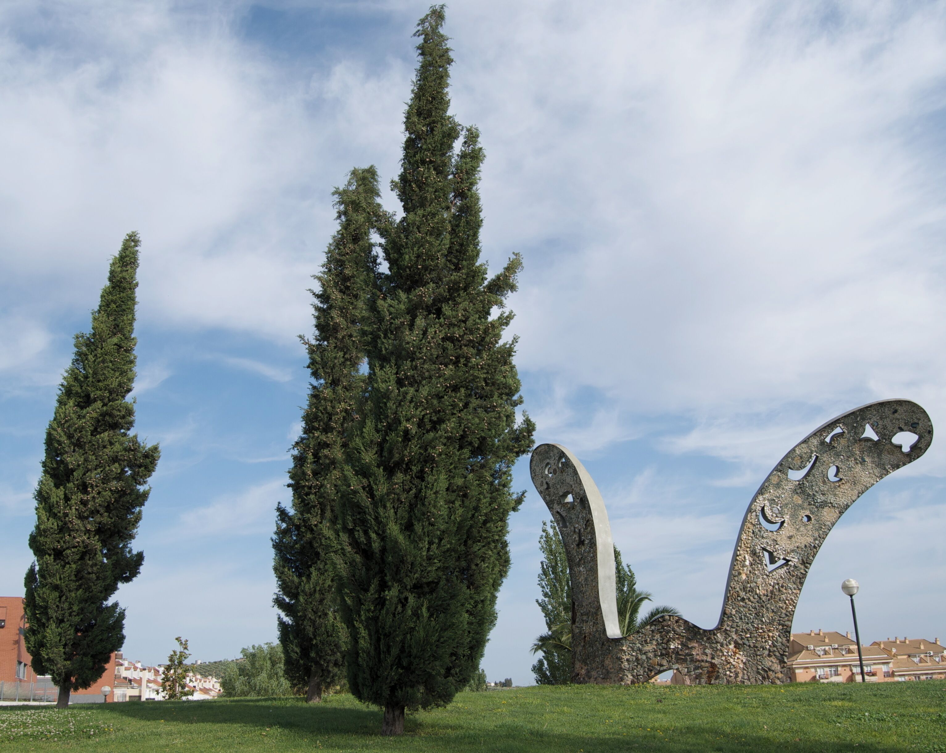 Un jardín de esculturas con altos cipreses y una gran escultura abstracta.