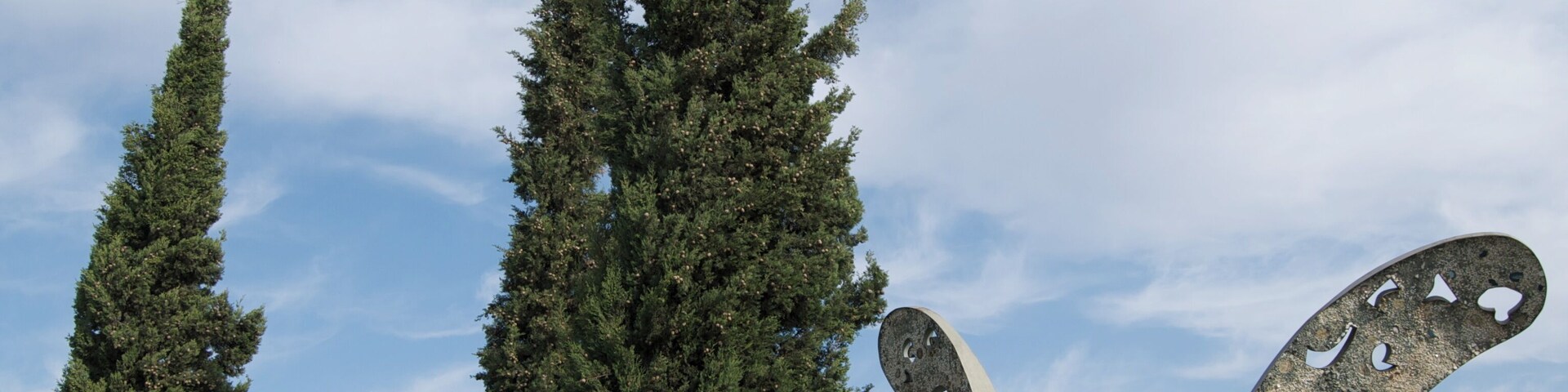 Un jardín de esculturas con altos cipreses y una gran escultura abstracta.