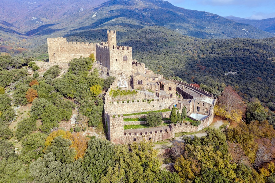 Un castillo medieval rodeado de colinas boscosas.