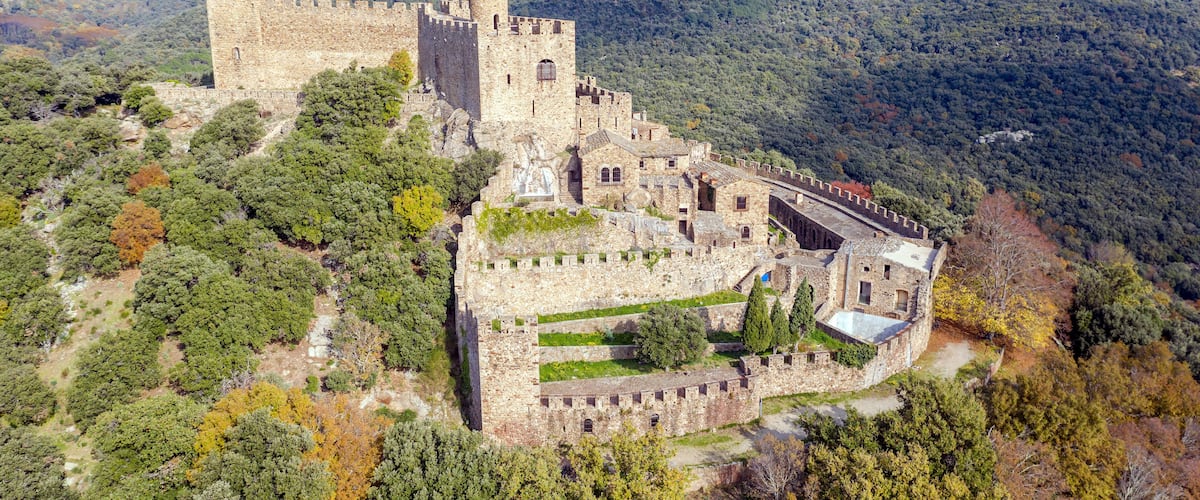 A medieval castle surrounded by forested hills.