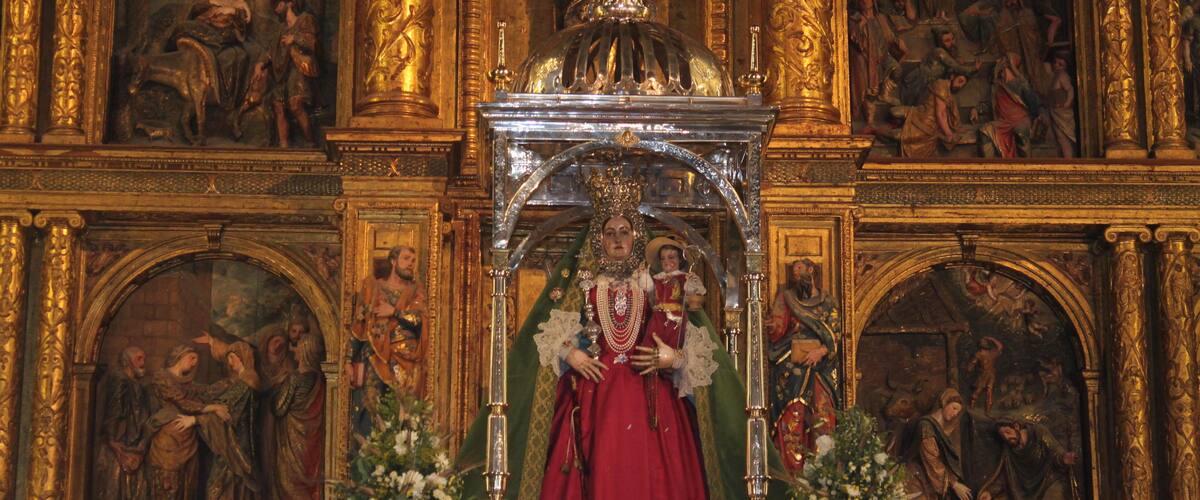 A religious statue with a red robe, surrounded by ornate gold decorations and floral arrangements.