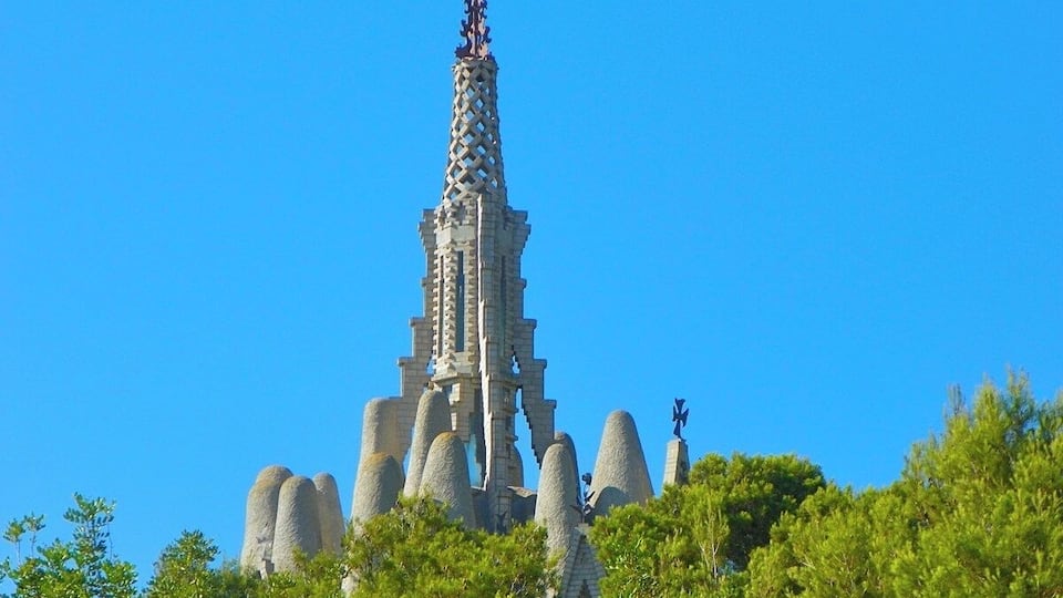 A tall, ornate tower with a spire, surrounded by lush green trees.