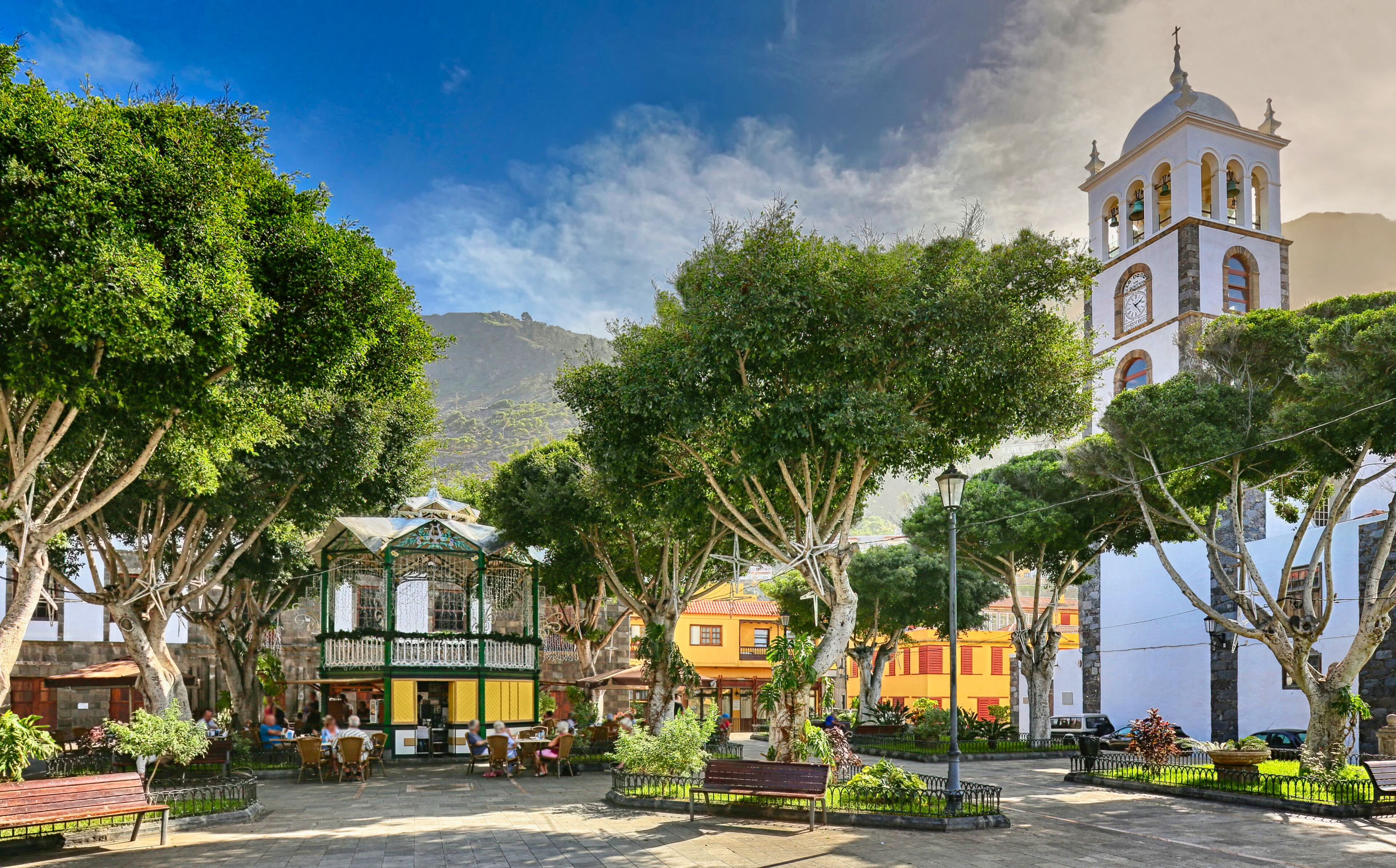 A plaza with a bell tower, trees, and buildings with outdoor seating.