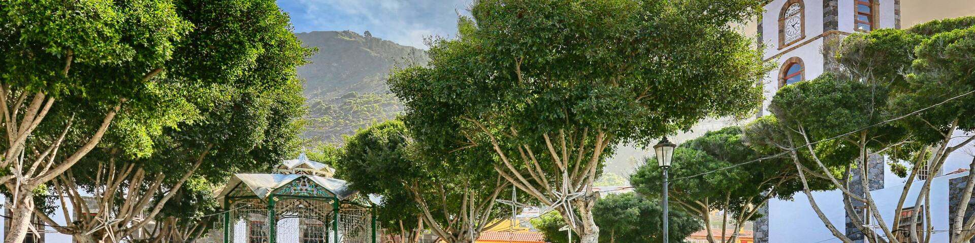 A plaza with a bell tower, trees, and buildings with outdoor seating.