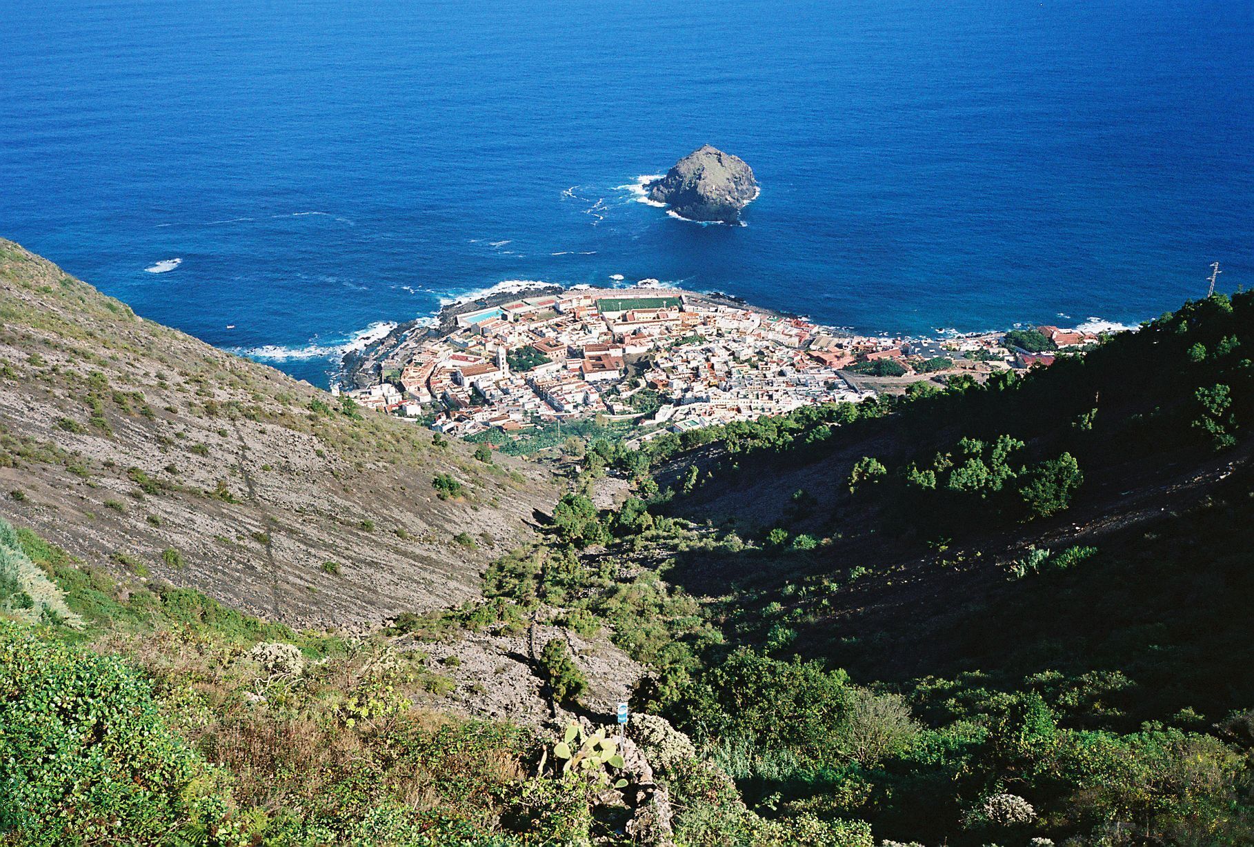A coastal town with a prominent hill and a small island in the background.