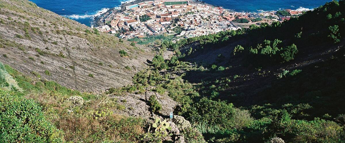 A coastal town with a prominent hill and a small island in the background.