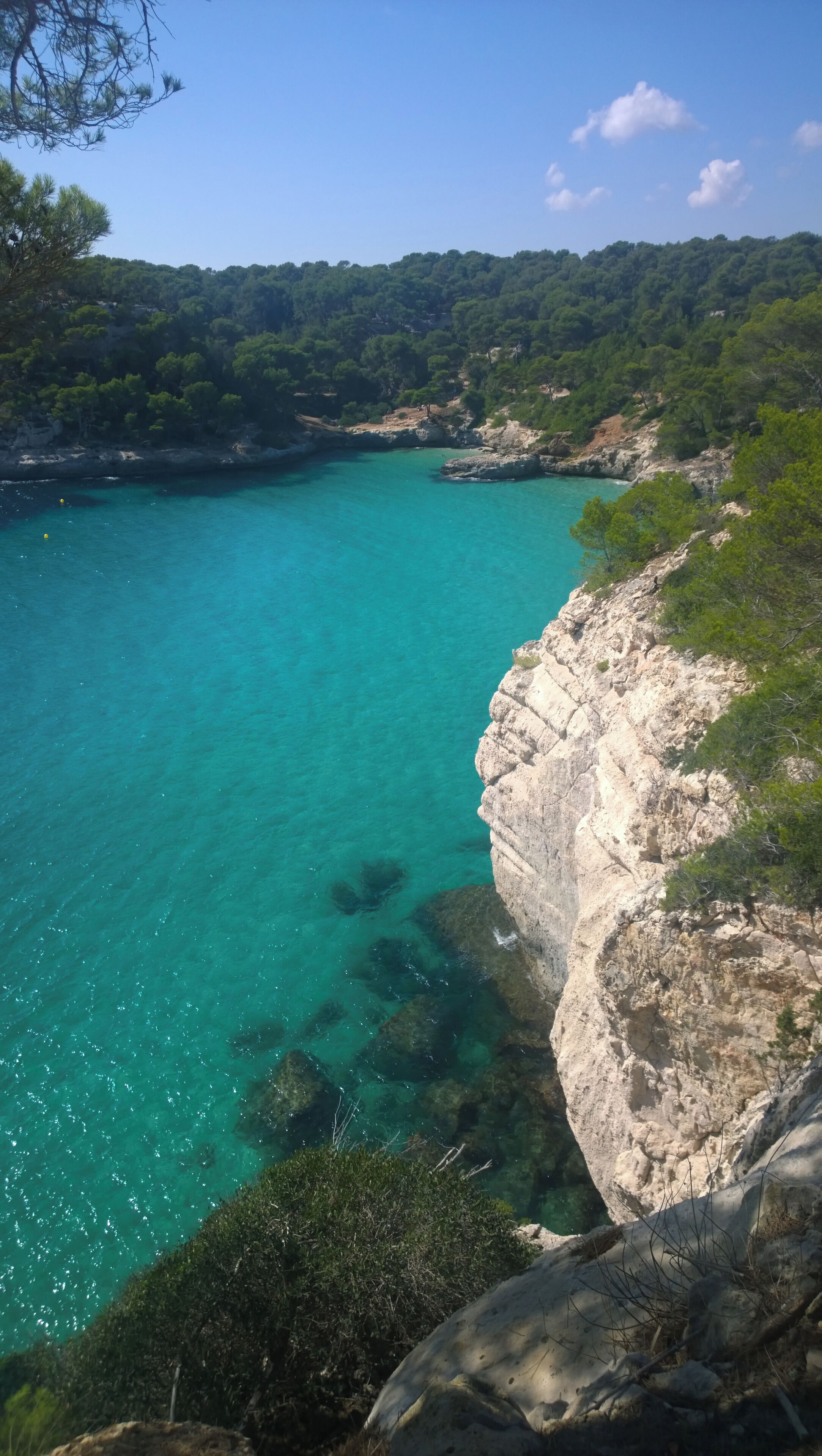 A coastal landscape with clear turquoise waters, rocky cliffs, and dense green vegetation.