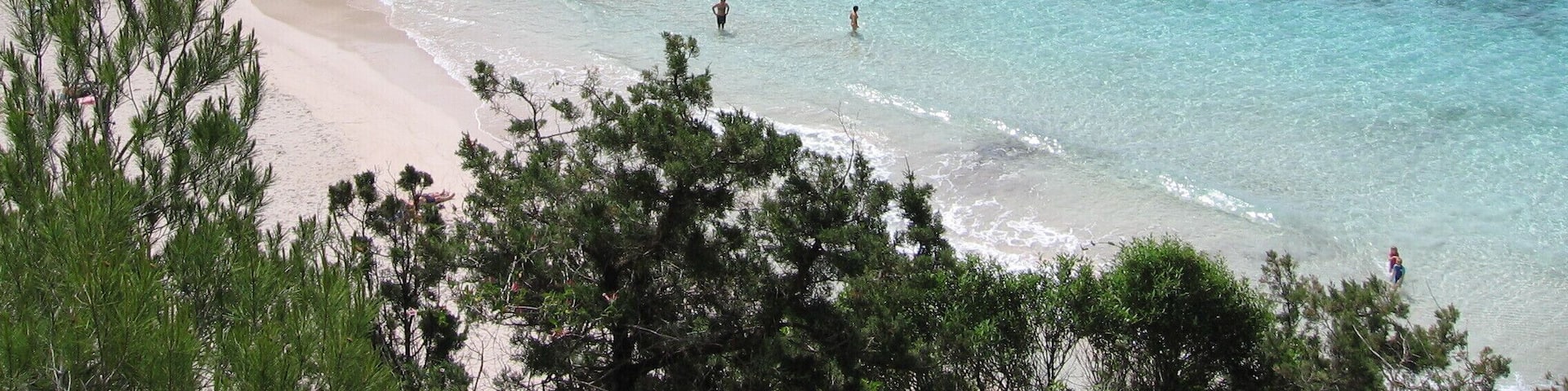 A coastal landscape with clear turquoise waters, a sandy beach, and rocky cliffs with sparse vegetation.