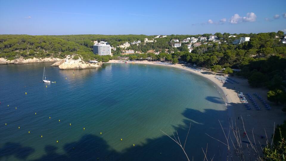 A coastal town with a beach, clear blue waters, and surrounding greenery.