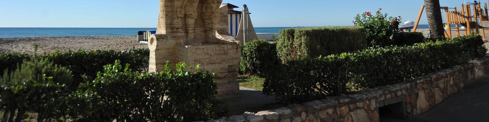 A stone statue, a palm tree, and a beach in the background.