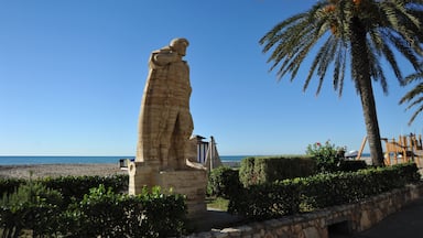 Uma estátua de pedra, uma palmeira e uma praia ao fundo.