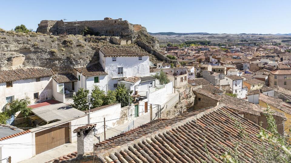 A town with historic architecture, a prominent fort on a hill, and a valley in the background.