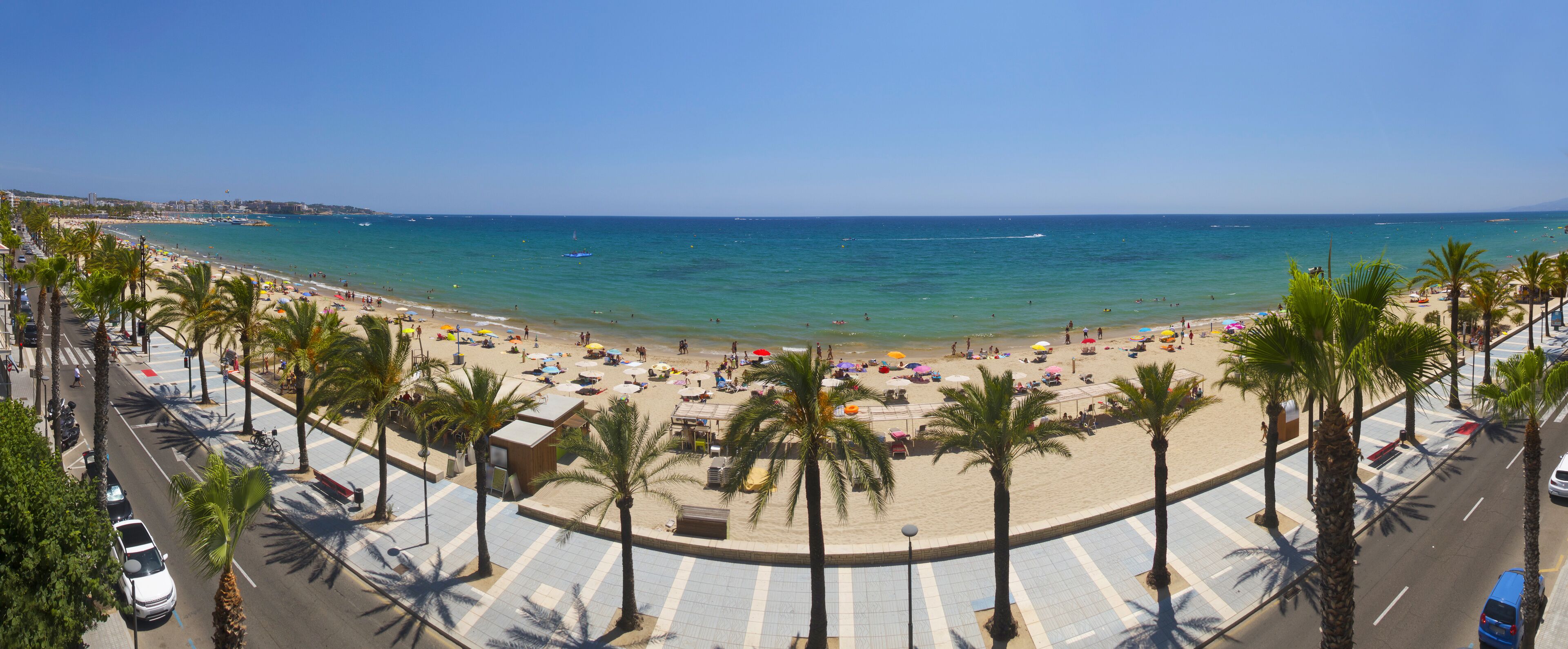 A beach with palm trees, umbrellas, and people.