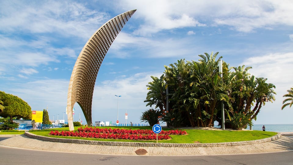 A curved architectural structure, a roundabout with a blue sign, and a large tree with red flowers.
