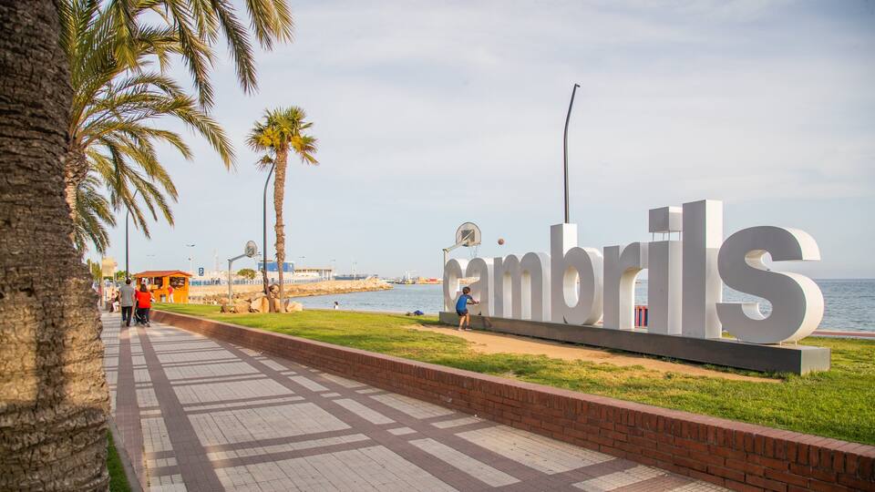 A coastal promenade with palm trees, a large 'Cambrils' sign, and a view of the sea.