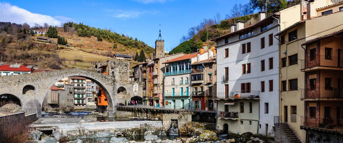 A historic town with a river, stone bridge, and colorful buildings.