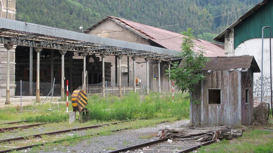 A dilapidated train station with overgrown vegetation and a small wooden structure.