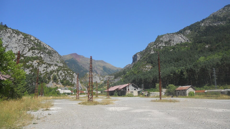 A rural landscape with a gravel road, a small building, and mountains in the background.