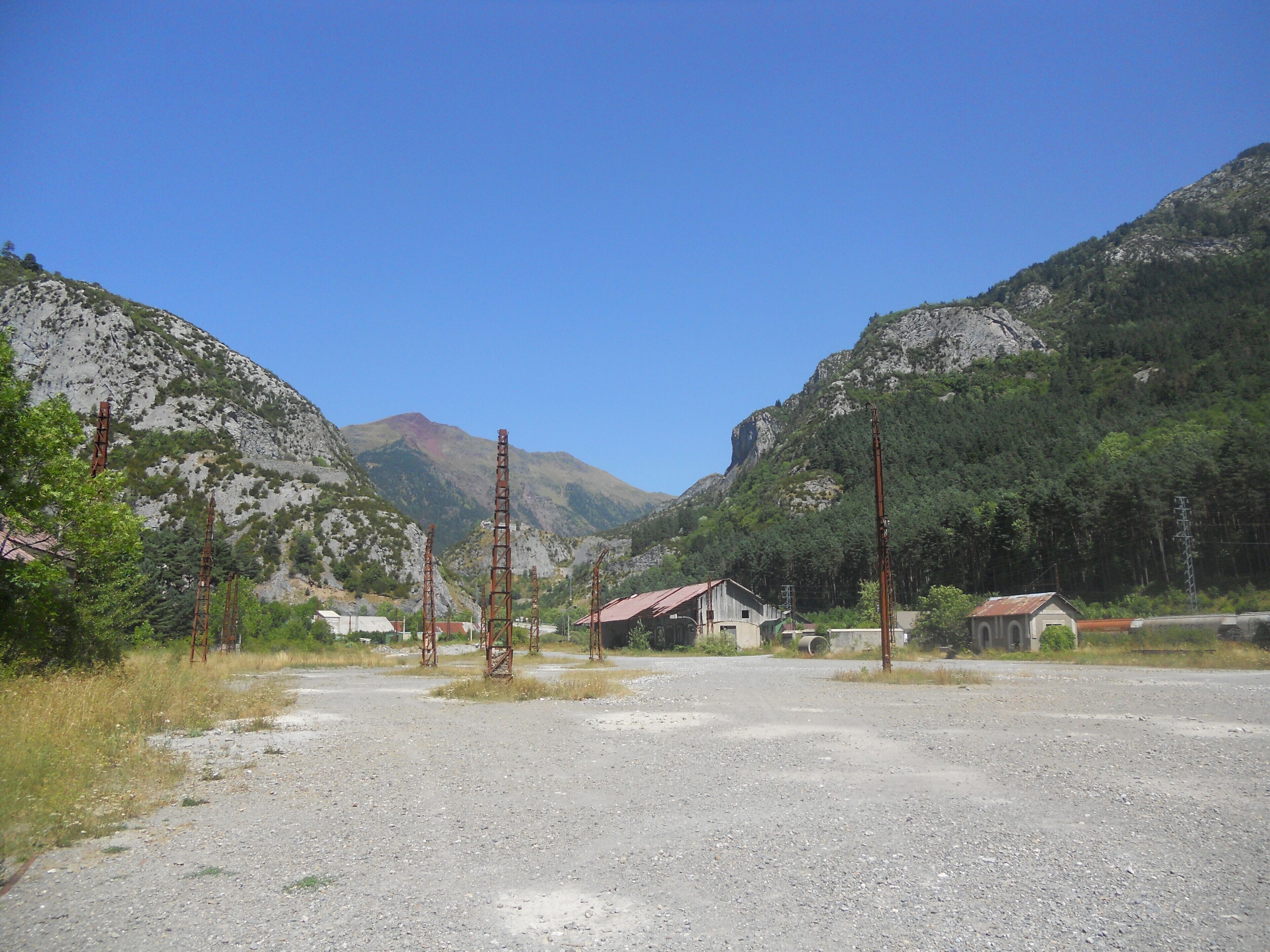 A rural landscape with a gravel road, a small building, and mountains in the background.