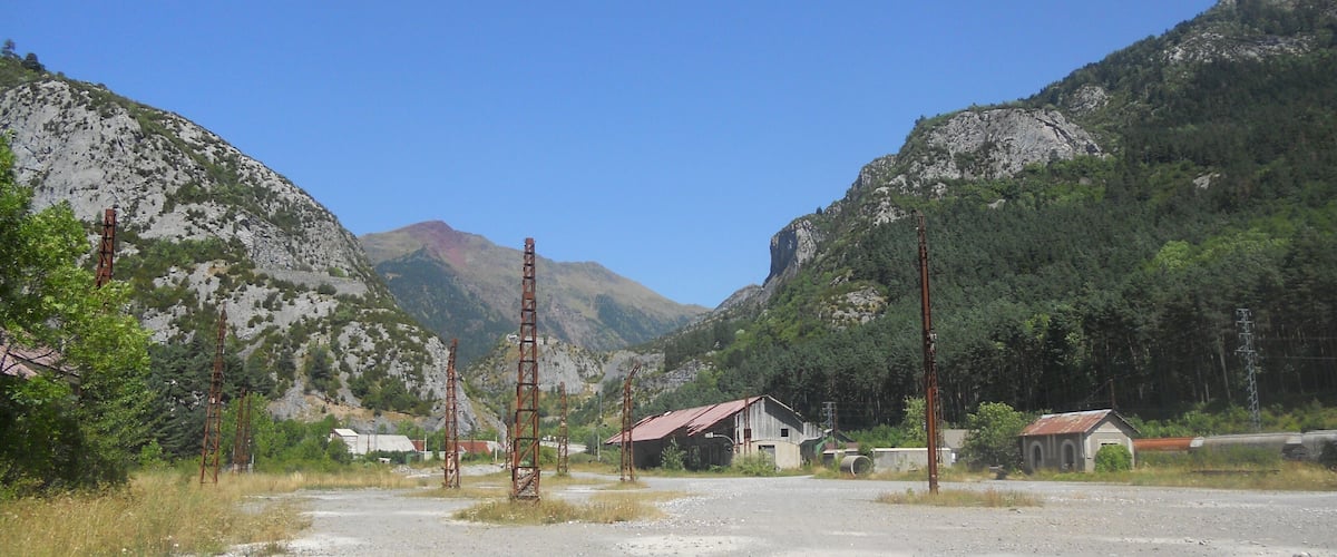A rural landscape with a gravel road, a small building, and mountains in the background.