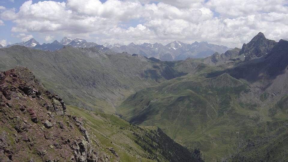 A mountainous landscape with green valleys and snow-capped peaks under a partly cloudy sky.