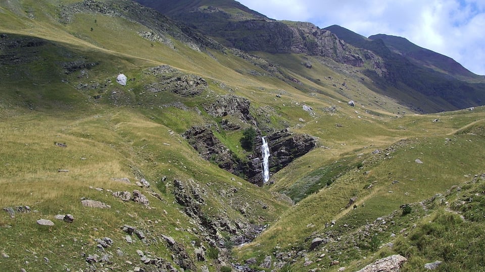 A mountainous landscape with a waterfall, rocky terrain, and grassy slopes.